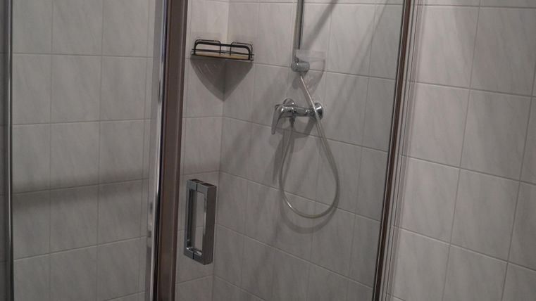 Eine moderne Dusche mit Glaswänden und grauen Fliesen. Der Raum ist hell und gut beleuchtet.