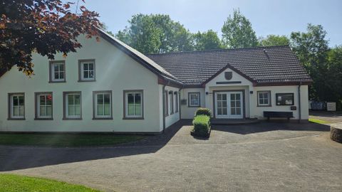 Ein modernes, zweigeschossiges Gebäude mit weißen Wänden und einem roten Dach. Es befindet sich in einer grünen Umgebung und wirkt einladend.