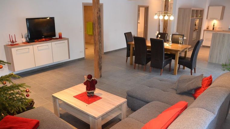 Ein modernes Wohnzimmer mit einer bequemen Couch und einem Holztisch. Der Raum ist gemütlich und gut beleuchtet, mit einem Essbereich und einem Fernseher in der Ecke.