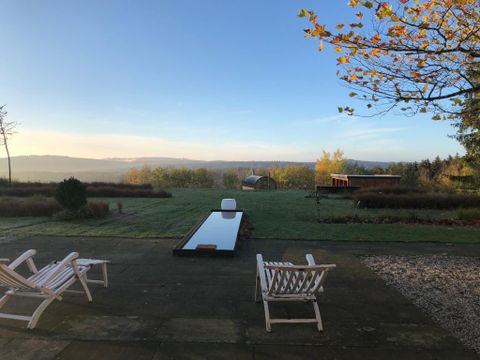 Eine ruhige Terrasse mit zwei Liegen und einem langen, spiegelnden Wasserbecken. Im Hintergrund erstreckt sich eine grüne Landschaft unter einem klaren Himmel.