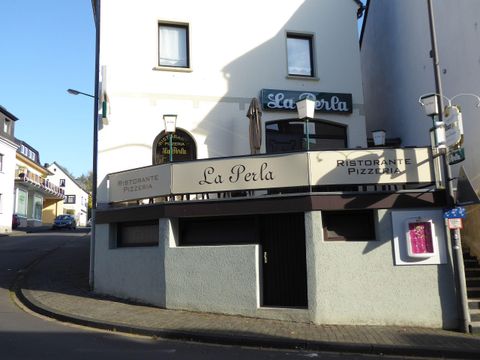 Een restaurant met de naam "La Perla" op een hoek van de straat. De gevel toont een moderne inrichting met een uitnodigende buitenruimte.