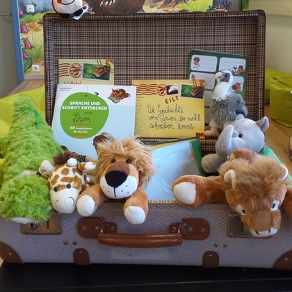 Ein Koffer voller Plüschtiere, darunter ein Löwe, eine Giraffe und ein Krokodil. Auf dem Koffer liegt eine Karte mit einer freundlichen Nachricht.