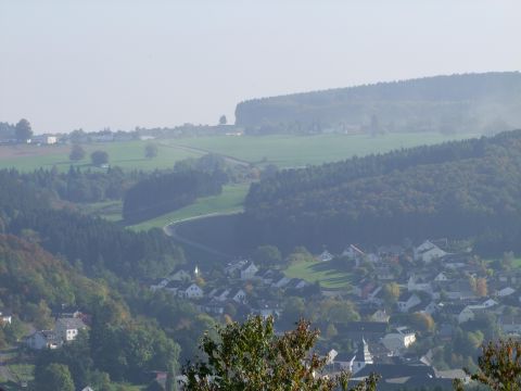 Eine malerische Landschaft mit sanften Hügeln und einem kleinen Dorf im Vordergrund. Die Umgebung ist grün und bewaldet, ideal für Naturliebhaber.