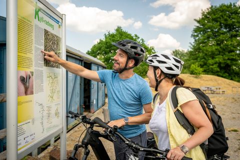 Zwei Radfahrer mit Helmen betrachten eine Infotafel am Kyll-Radweg.
