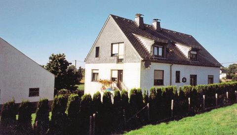 Ein schönes Haus mit einem grauen Dach und einem gepflegten Garten. Bäume und Sträucher umgeben das Grundstück.