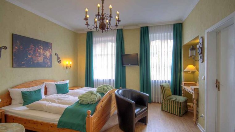 Ein gemütliches Schlafzimmer mit einem Doppelbett und hellgrünen Vorhängen. Der Raum ist geschmackvoll eingerichtet und verfügt über einen Fernseher sowie einen Schreibtisch.