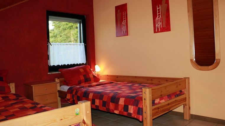 Ein gemütliches Schlafzimmer mit zwei Einzelbetten und bunten Bettwäsche in Rot und Blau. Die Wände sind in warmen Farben gestrichen und mit einfachen Dekorationen versehen.