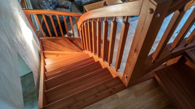Eine schöne Holztreppe mit einer sanften Kurve. Das Licht fällt warm auf die Stufen und den Geländer.