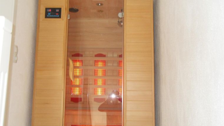 Eine moderne Infrarot-Sauna aus Holz mit einer gläsernen Vorderseite. Im Inneren sind leuchtende Infrarotstrahler sichtbar.