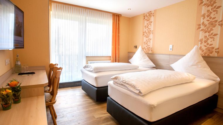 Ein helles Zimmer mit zwei Einzelbetten und einem Tisch. Große Fenster lassen viel Tageslicht herein.