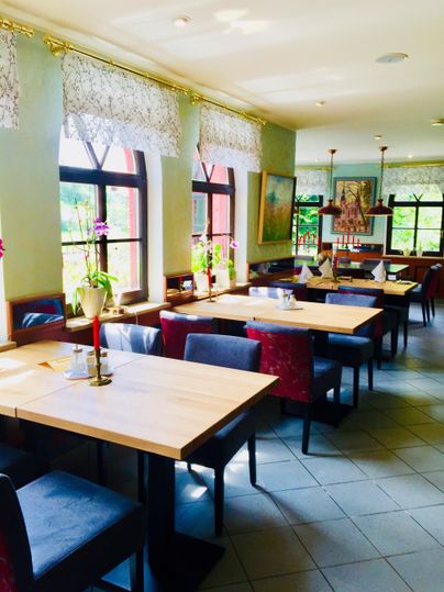 Ein helles Restaurant mit eleganten Tischen und Stühlen. Blumen schmücken die Tische und große Fenster bieten einen Blick nach draußen.