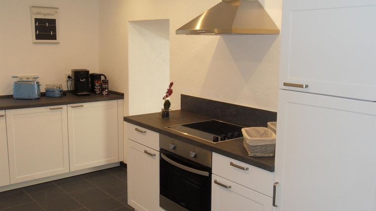 Eine moderne Küche mit weißen Möbeln und dunkler Arbeitsplatte. Sie ist gut ausgestattet mit einem Herd, einem Kühlschrank und einer Kaffeemaschine.