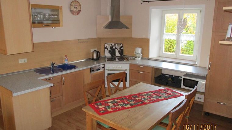 Eine moderne Küche mit Holzmöbeln und einem großen Esstisch. Der Raum ist hell und freundlich, mit einem Fenster, das auf den Garten blickt.