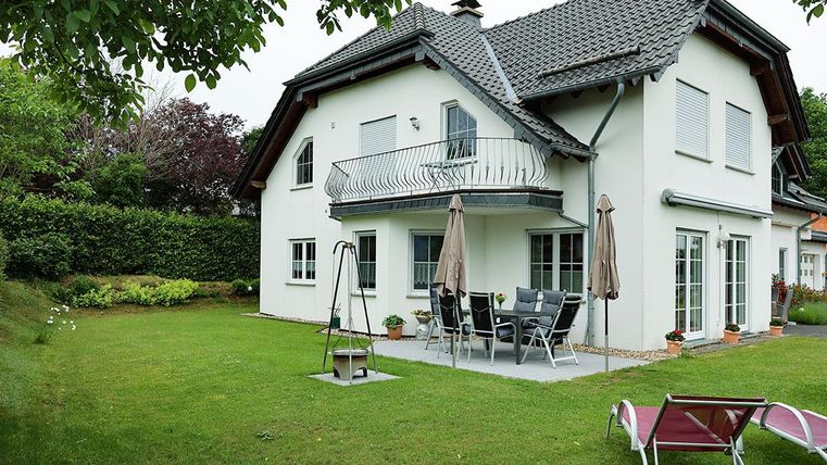 Ein modernes Haus mit einem gepflegten Garten. Auf der Terrasse stehen Möbel und Sonnenschirme.