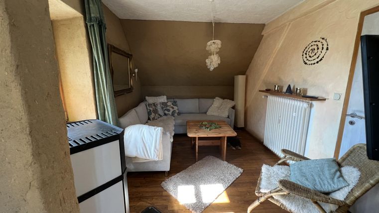 Ein gemütliches Wohnzimmer mit einer grauen Couch und einem Holztisch. Das Licht fällt durch das Fenster und schafft eine einladende Atmosphäre.