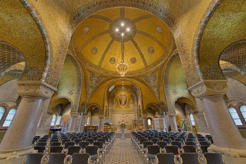 Interior view of the Church of the Redeemer in Gerolstein with an elaborate mosaic ceiling, chandelier, and rows of seats. A large circular window and altar are visible.