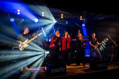 Une bande se produit en direct sur scène. Des lumières colorées brillent et les musiciens créent une atmosphère énergique.