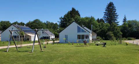 Ein grüner Garten mit modernen Häusern im Hintergrund. Auf dem Spielplatz stehen Schaukeln und eine Bank.