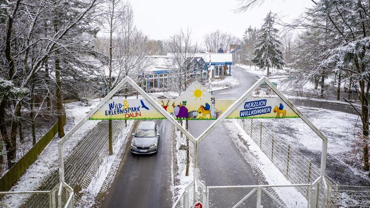 Une entrée d'un parc d'attractions dans la neige. Un panneau de bienvenue et une voiture sont visibles.