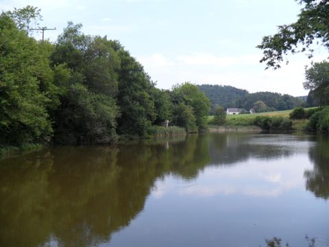 Un fleuve tranquille entouré d'arbres verts et d'une douce colline à l'arrière-plan. La surface de l'eau reflète le paysage.