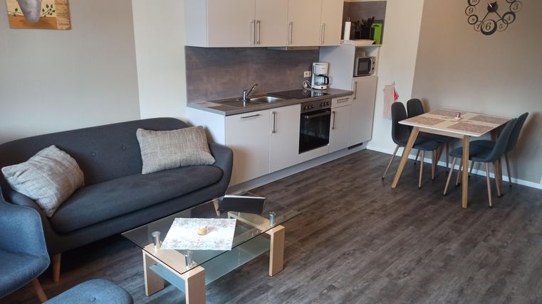 Eine moderne Wohnzimmerküche mit einem grauen Sofa, einem Tisch und Stühlen. Die Einrichtung ist hell und einladend.