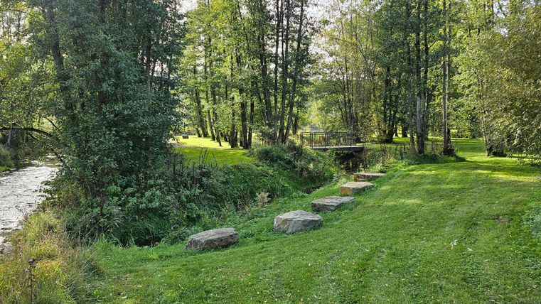 Green park with trees, a small river, and a bridge in the Kurpark Stadtkyll. Stones line the path along the water.