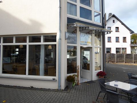 Ein schönes Café an einer ruhigen Straße mit großen Fenstern. Draußen stehen Tische und Stühle für Gäste.