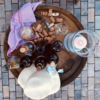 Ein rustikaler Tisch mit verschiedenen Weinflaschen, Gläsern und Korken. Dazu liegen ein Hütchen und ein Tuch in einem lässigen Ambiente.