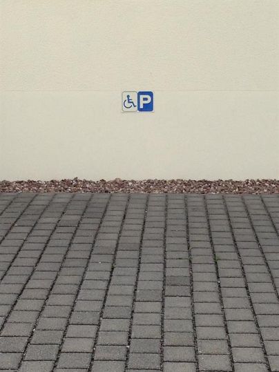 Ein Parkplatz für Menschen mit Behinderungen ist ausgeschildert. Der Boden besteht aus rechteckigen Steinen.