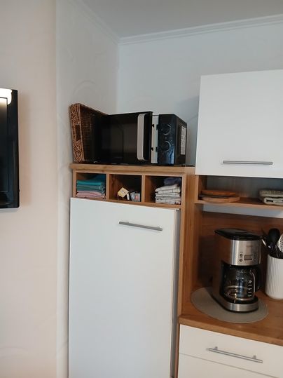 Eine moderne Küche mit einem Kühlschrank und einer Mikrowelle auf einem Regal. Darunter steht eine Kaffeemaschine und einige Küchenutensilien sind sichtbar.
