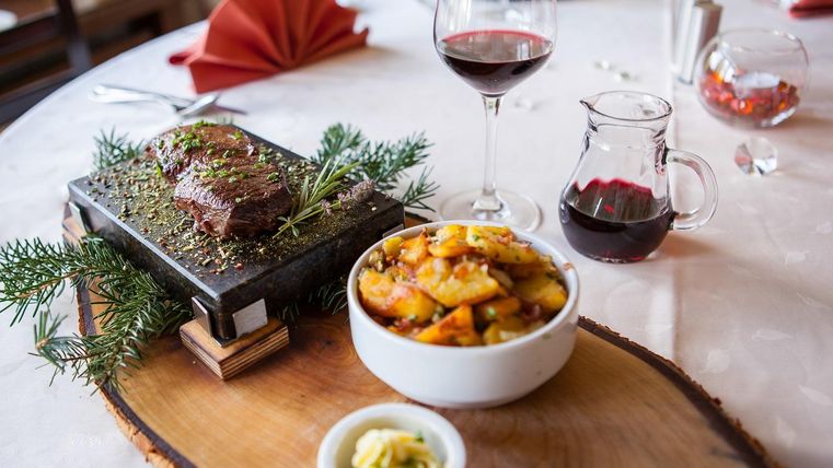 Ein leckeres Steak auf einem heißen Stein mit Kräutern, begleitet von einer Schüssel mit gedünstetem Gemüse. Ein Glas Rotwein rundet das Gericht ab.