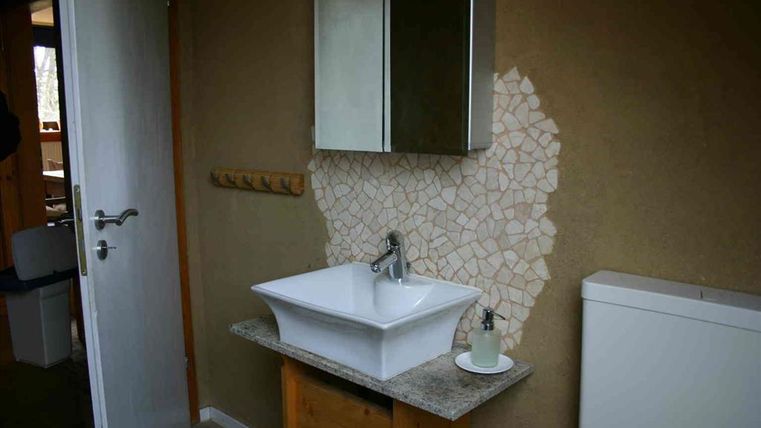 Ein modern gestaltetes Badezimmer mit einem weißen Waschtisch und einem Spiegel. Die Wand hat teilweise eine kreative Mosaikverkleidung.