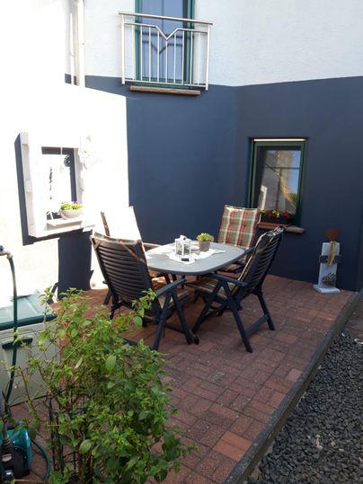 Ein gemütlicher Innenhof mit einem Tisch und Stühlen. Die Wände sind in zwei Farben gestrichen, und einige Pflanzen verleihen dem Raum eine lebendige Note.