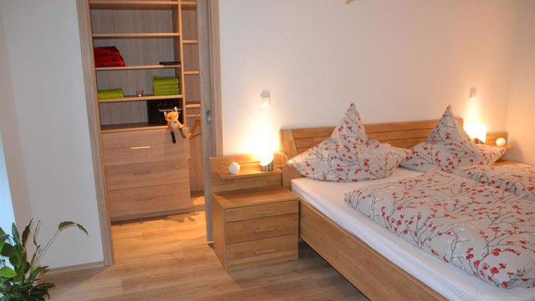 Ein helles Schlafzimmer mit einem großen Bett und dekorativen Kissen. Im Hintergrund befindet sich ein offener Schrank mit ordentlichen Regalen.