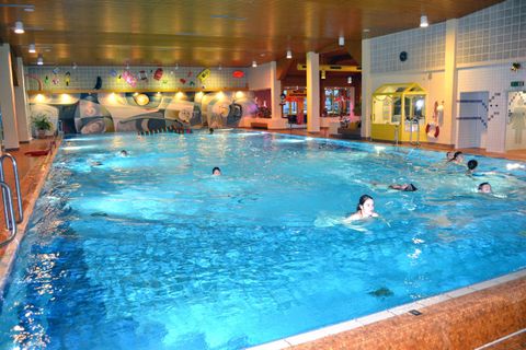 Ein Schwimmbad mit klarem Wasser und mehreren Schwimmern. Im Hintergrund sind bunte Wände und Einrichtungen zu sehen.