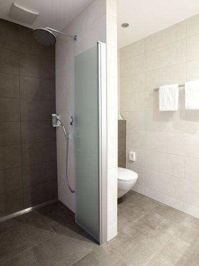 Ein modernes Badezimmer mit einer Dusche und einer Toilette. Helle Fliesen und handtücher verleihen dem Raum eine saubere Atmosphäre.