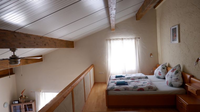 Ein gemütliches Schlafzimmer mit einem Doppelbett und holzverkleideten Wänden. Viel natürliches Licht fällt durch das Fenster und sorgt für eine einladende Atmosphäre.