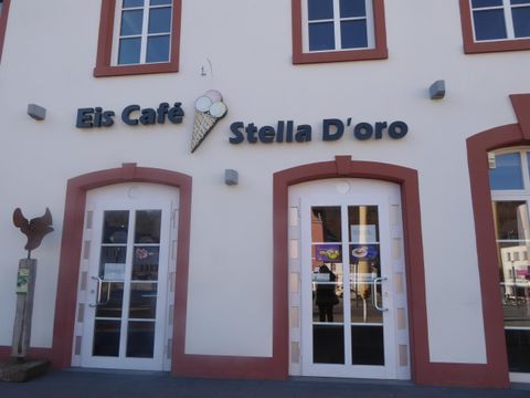 Ein Café mit dem Namen "Eis Café Stella D'oro". Die Fassade zeigt große Fenster und ein elegantes Design.