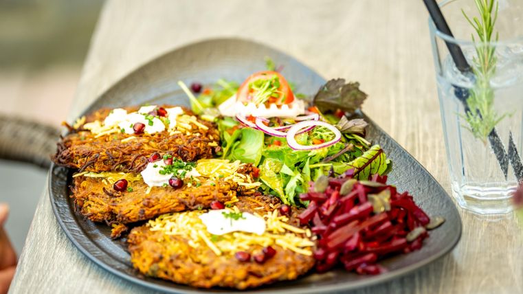 Ein ansprechender Teller mit knusprigen Kartoffelrösti, frischem Salat und Rote-Bete-Beilage. Das Gericht ist dekorativ angerichtet und sieht sehr appetitlich aus.
