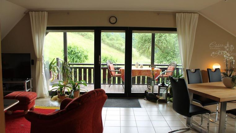 Ein gemütliches Wohn- und Esszimmer mit einem großen Fenster und Blick auf eine grüne Landschaft. Es gibt einen Esstisch und bequeme Möbel, die zum Entspannen einladen.