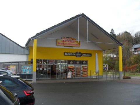 Ein Discounter-Markt mit gelber Fassade und einem großen Eingang. Vor dem Gebäude stehen parkende Autos.