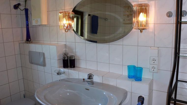 Ein helles Badezimmer mit einem modernen Waschbecken und einem großen Spiegel. Die Wände sind gefliest, und es gibt verschiedene dekorative Elemente in blau und schwarz.