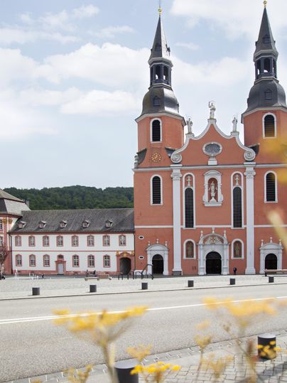 Une église magnifique avec deux tours et une façade impressionnante se dresse au premier plan. À l'arrière-plan, on aperçoit des collines douces et un ciel bleu.