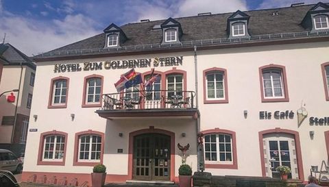 Das Bild zeigt das Hotel "Zum Goldenen Stern" mit einem gemütlichen Eingang und einem Balkon. Über dem Eingang hängen mehrere Flaggen.