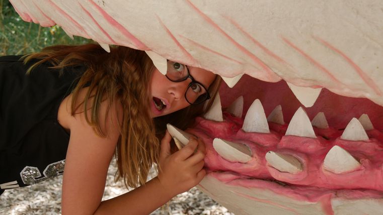 Une fille avec des lunettes pose dans un modèle artistique de la bouche d'un requin. Elle a l'air surprise en sortant de la bouche du requin.