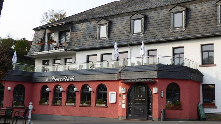 Ein charmantes Hotel mit roter Fassade und einem Balkon. Die Umgebung wirkt einladend und gepflegt.