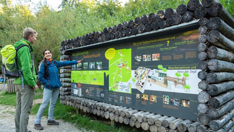 A couple stands in front of an information board in the forest. The board displays a map and information about the surroundings and activities.