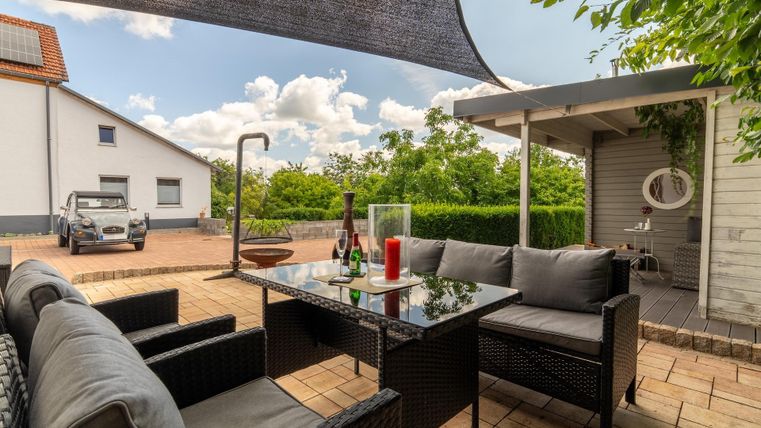 Ein gemütlicher Außenbereich mit einem schwarzen Rattan-Sofa und einem Tisch. Im Hintergrund ist ein gepflegter Garten und eine helle, freundliche Atmosphäre zu sehen.