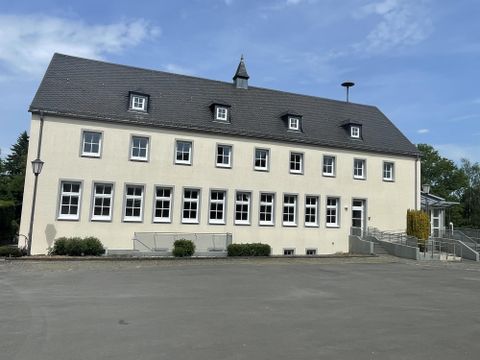 Un grand bâtiment de deux étages avec une façade jaune et de nombreuses fenêtres. Le ciel est clair et bleu, et il y a quelques voitures devant.