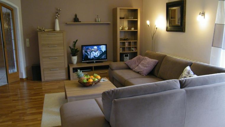 Ein gemütliches Wohnzimmer mit einem großen, beigen Sofa und einem Fernseher. Der Raum hat Holzfußboden und eine ruhige, einladende Atmosphäre.